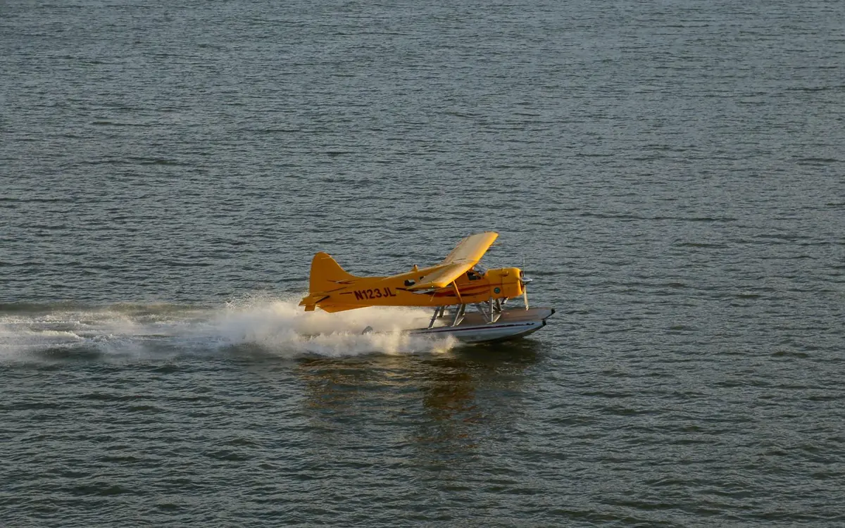 Um hidroavião amarelo na água levantando spray ao descolar