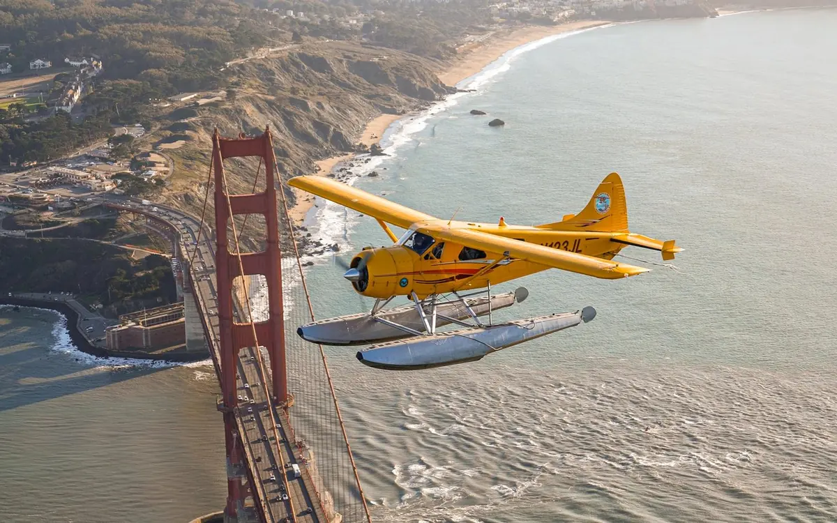Ein Wasserflugzeug auf Schwimmern fliegt über die San Francisco Bay, dahinter die Skyline der Stadt